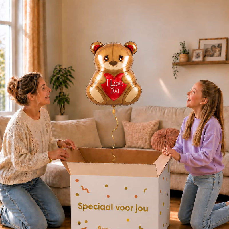 Moeder en meisje bekijken een beertjesballon van 45 cm met een rood I Love You-hart boven een geopende cadeaudoos.