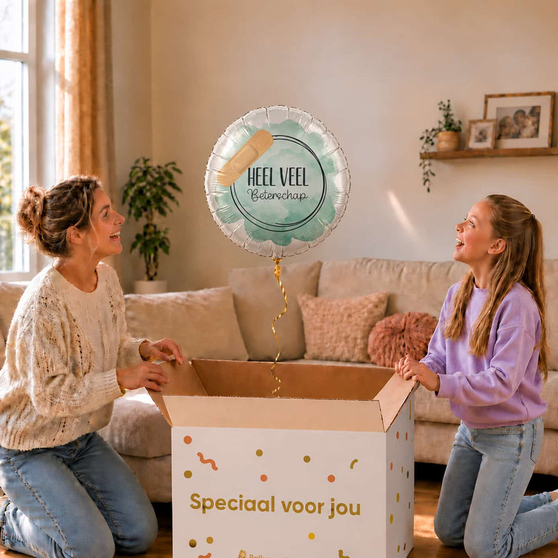 Moeder en meisje bekijken een mintgroene Heel Veel Beterschap-ballon van 43 cm met een pleister boven een geopende cadeaudoos.