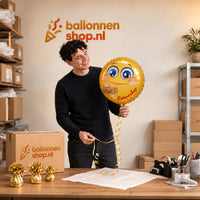 Jesse houdt de Smiley beterschap ballon vast in de warme werkplaats van Ballonnenshop.nl.