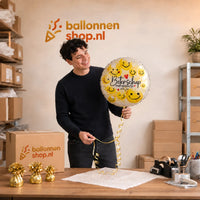 Jesse houdt de Beterschap Smiley Opkikker Ballon vast in de warme werkplaats van Ballonnenshop.nl.