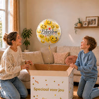 Moeder en jongen bekijken een Beterschap Smiley Opkikker-ballon van 43 cm met gele smileys boven een geopende cadeaudoos.