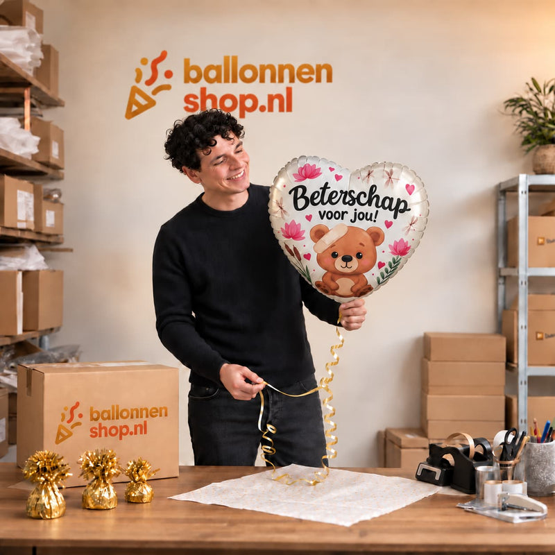 Een medewerker houdt de hartvormige Beterschap voor jou-ballon met beertje, pleister en bloemen vast bij de inpaktafel.