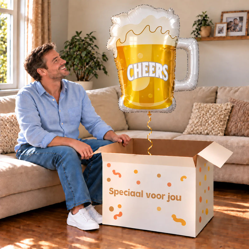 Een man kijkt blij naar Bier Helium XL Ballon Cheers boven een grote Speciaal voor jou-doos in een warme woonkamer.