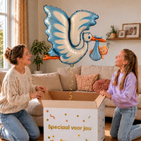 Blauwe Ooievaar Helium XL Ballon zweeft boven een geopende cadeaudoos bij een moeder en meisje in een warme woonkamer.