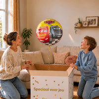 Moeder en jongen bekijken een Cars Racers-ballon van 46 cm met Lightning McQueen en Jackson Storm boven een geopende cadeaudoos.