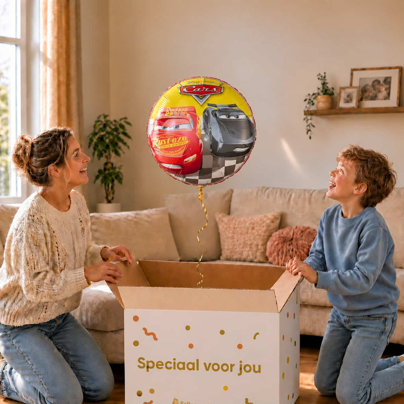 Moeder en jongen bekijken een Cars Racers-ballon van 46 cm met Lightning McQueen en Jackson Storm boven een geopende cadeaudoos.