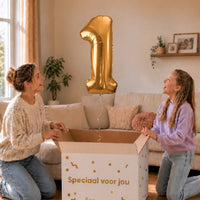 Cijfer 1 Helium Ballon Goud zweeft boven een geopende cadeaudoos bij een moeder en meisje in een warme woonkamer.