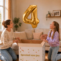 Cijfer 4 Helium Ballon Goud zweeft boven een geopende cadeaudoos bij een moeder en meisje in een warme woonkamer.