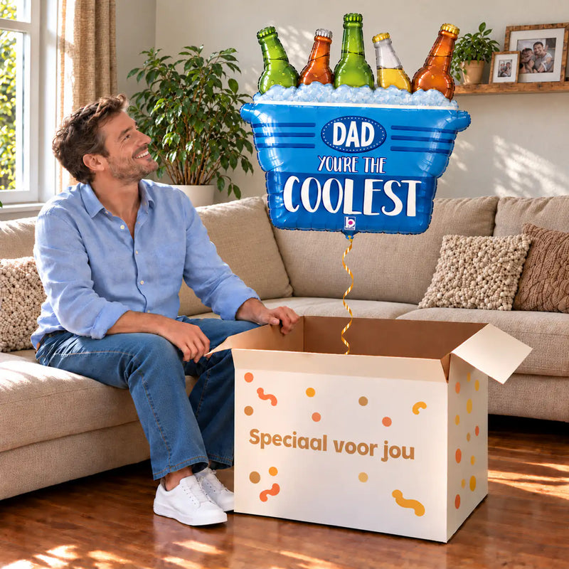 Een man kijkt blij naar Dad You're The Coolest XL Ballon boven een grote Speciaal voor jou-doos in een warme woonkamer.