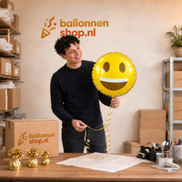 Jesse houdt de Emoji Glimlach Helium Ballon vast in de warme werkplaats van Ballonnenshop.nl.