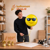 Jesse houdt de Emoji Zonnebril Helium Ballon vast in de warme werkplaats van Ballonnenshop.nl.