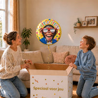 Moeder en jongen bekijken een gele Gefeliciteerd-heliumballon van 46 cm met een aap met rode zonnebril boven de cadeaudoos.