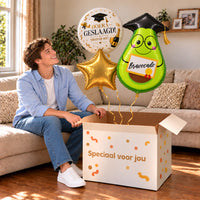 Een blije geslaagde met Geslaagd Bravocado Ballonnentros boven een open Speciaal voor jou-doos in een warme woonkamer.