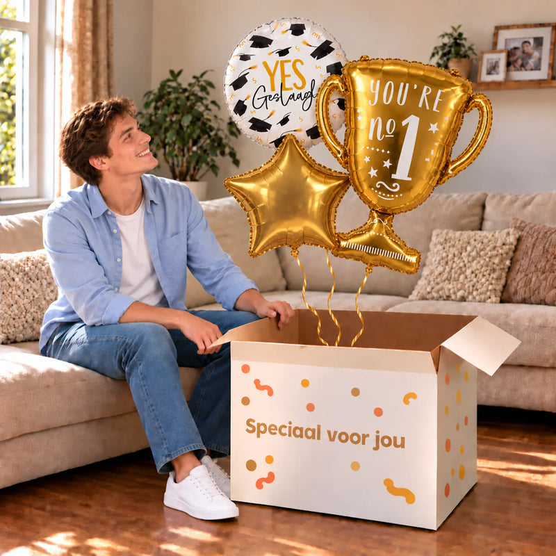 Een blije geslaagde met Geslaagd Trofee Ballonnentros boven een open Speciaal voor jou-doos in een warme woonkamer.