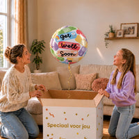 Moeder en meisje bekijken een Get Well Soon heliumballon van 45 cm met kleurrijke pleisters boven de cadeaudoos.