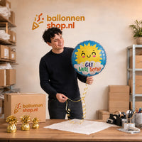 Jesse houdt de Get Well Soon Zon Helium Ballon vast in de warme werkplaats van Ballonnenshop.nl.