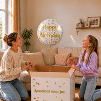 Moeder en meisje bekijken een witte Happy Birthday heliumballon van 46 cm met bloemen en gouden letters boven de cadeaudoos.