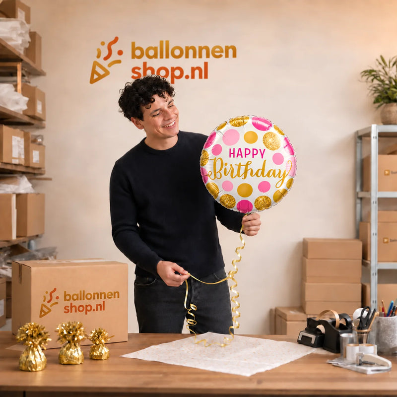 Jesse houdt de Happy Birthday Roze Goud ballon vast in de warme werkplaats van Ballonnenshop.nl.