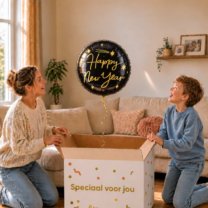 Moeder en jongen kijken naar een zwarte Happy New Year heliumballon met gouden letters en sterren boven een geopende cadeaudoos.
