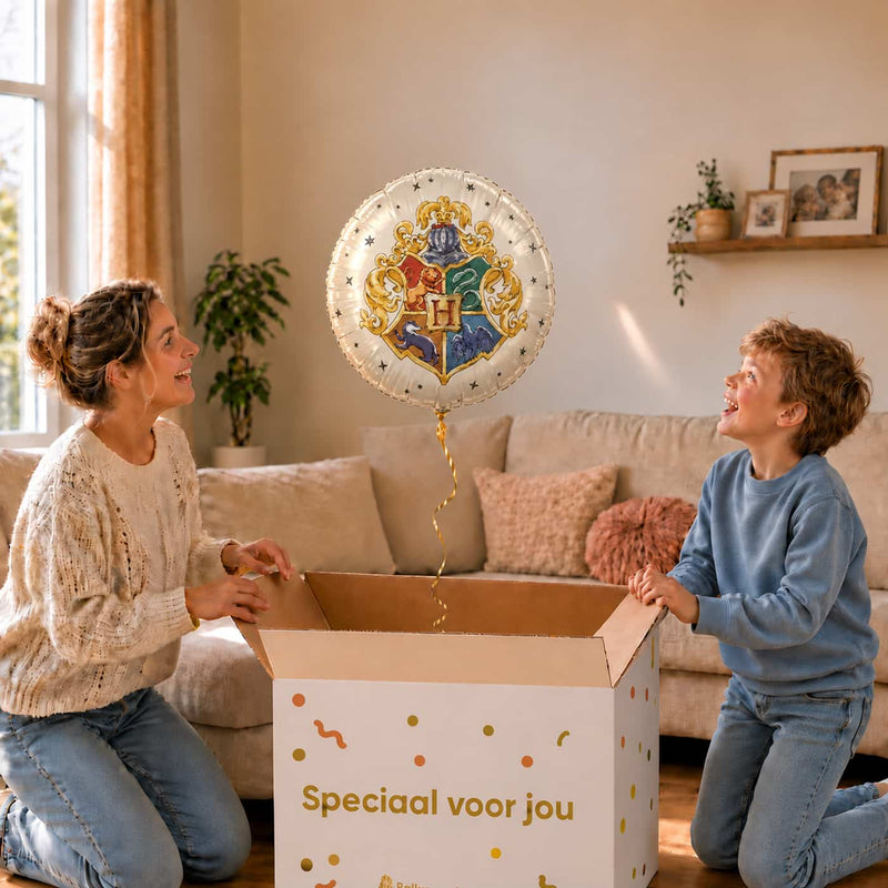 Moeder en jongen bekijken een Harry Potter heliumballon met het wapen van Zweinstein boven de open cadeaudoos.