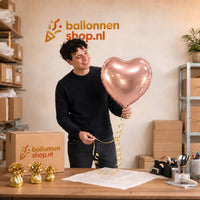 Jesse houdt de Hart Ballon Rose Goud – 46 cm vast in de warme werkplaats van Ballonnenshop.nl.