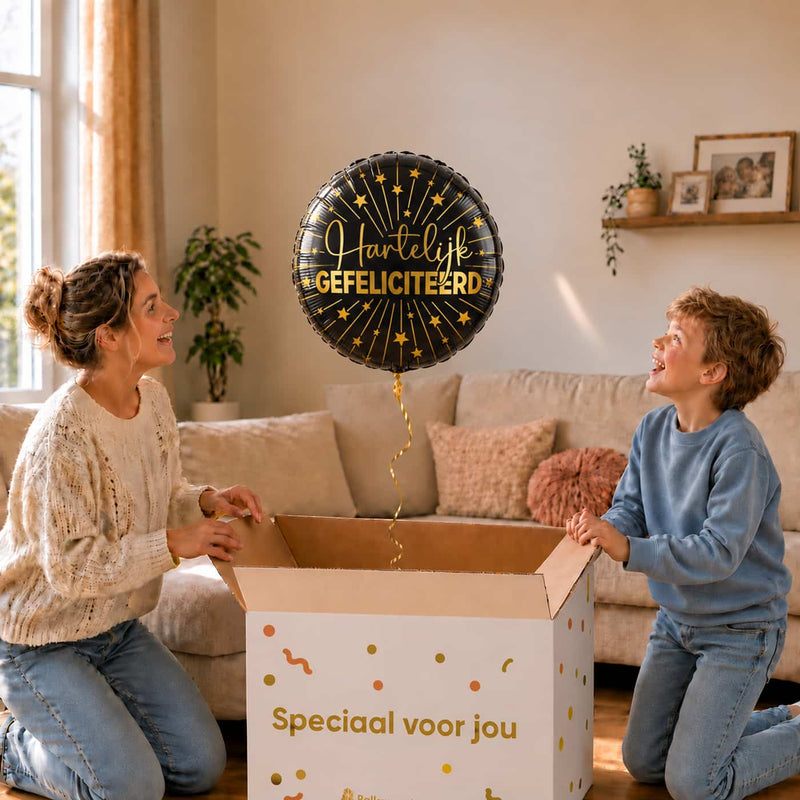 Moeder en jongen bekijken een zwarte Hartelijk Gefeliciteerd heliumballon met gouden sterren boven de geopende cadeaudoos.