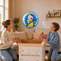 Moeder en jongen bekijken een blauwe Bumba heliumballon met Bumba en zijn gitaar boven de geopende cadeaudoos.