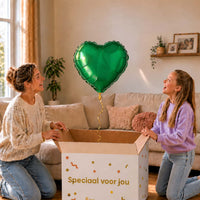 Moeder en meisje bekijken een effen groene hartvormige heliumballon boven de geopende cadeaudoos.