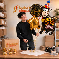 Jesse houdt het Holy Cow Birthday XL Trosje met grote koe, gouden ster en felicitatieballon vast in de warme werkplaats van Ballonnenshop.nl
