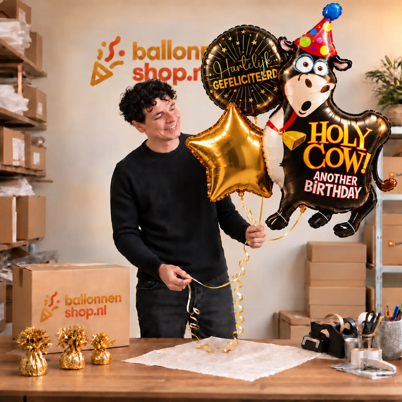 Jesse houdt het Holy Cow Birthday XL Trosje met grote koe, gouden ster en felicitatieballon vast in de warme werkplaats van Ballonnenshop.nl