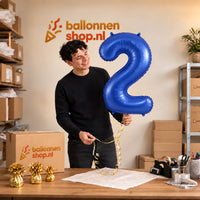 Jesse houdt de 2 Jaar Cijfer Mat Blauw XL vast in de warme inpakruimte van Ballonnenshop.nl.