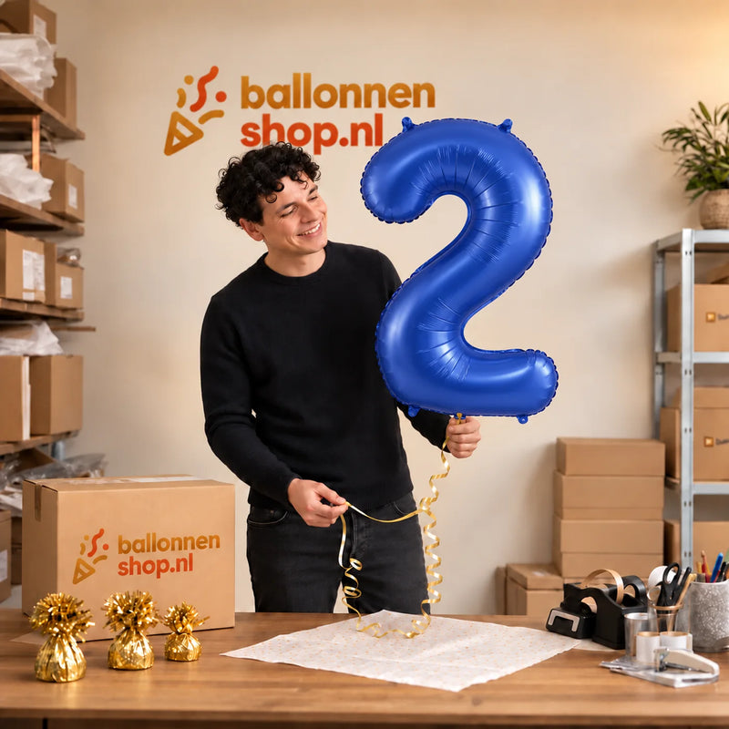 Jesse houdt de 2 Jaar Cijfer Mat Blauw XL vast in de warme inpakruimte van Ballonnenshop.nl.