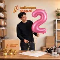 Jesse houdt de 2 Jaar Cijfer Mat Roze XL Ballon vast in de warme inpakruimte van Ballonnenshop.nl.