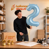 Jesse houdt de 2 Jaar Cijfer Pastel Blauw XL vast in de warme inpakruimte van Ballonnenshop.nl.