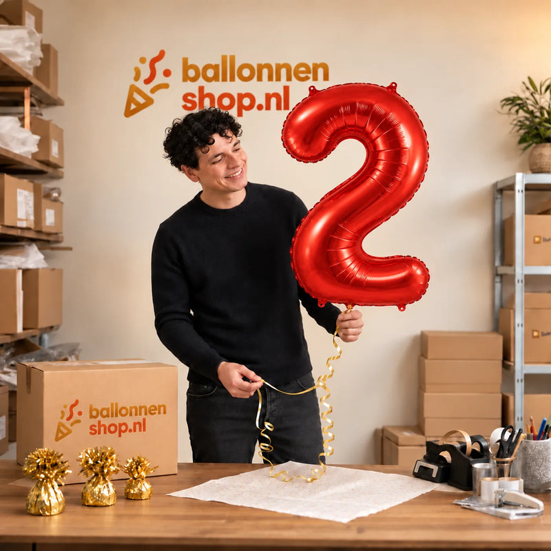Jesse houdt de 2 Jaar Cijfer Rood XL Ballon vast in de warme inpakruimte van Ballonnenshop.nl.