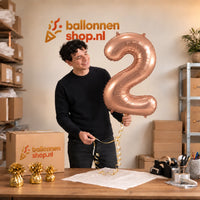 Jesse houdt de 2 Jaar Cijfer Rose Goud XL vast in de warme inpakruimte van Ballonnenshop.nl.