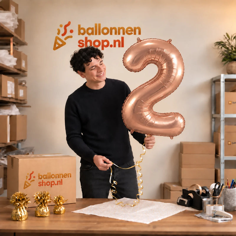 Jesse houdt de 2 Jaar Cijfer Rose Goud XL vast in de warme inpakruimte van Ballonnenshop.nl.