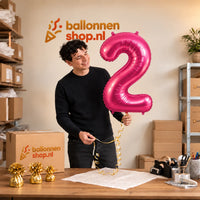 Jesse houdt de 2 Jaar Cijfer Roze XL Ballon vast in de warme inpakruimte van Ballonnenshop.nl.