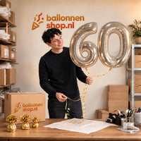 Jesse houdt de 60 Jaar Cijfer Ballonnen Zilver vast in de warme inpakruimte van Ballonnenshop.nl.
