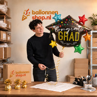 Jesse houdt de Congrats Grad Afstudeerhoed Ballon vast in de warme inpakruimte van Ballonnenshop.nl.