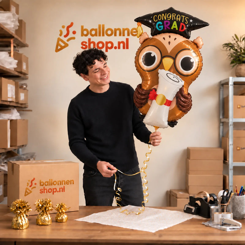 Jesse houdt de Congrats Grad Uil Ballon vast in de warme inpakruimte van Ballonnenshop.nl.