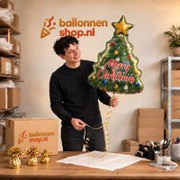 Jesse houdt de Kerstboom Merry Christmas XL vast in de warme inpakruimte van Ballonnenshop.nl.