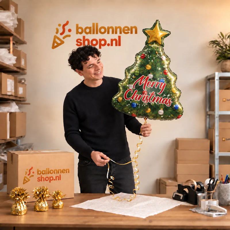 Jesse houdt de Kerstboom Merry Christmas XL vast in de warme inpakruimte van Ballonnenshop.nl.