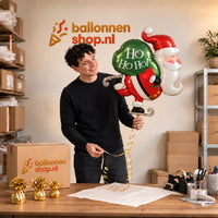 Jesse houdt de Kerstman Ho Ho Ho! XL Ballon vast in de warme inpakruimte van Ballonnenshop.nl.