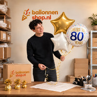 Jesse houdt 80 Jaar Trosje Wit/Goud/Blauw vast in de warme werkplaats van Ballonnenshop.nl.