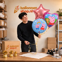 Jesse houdt Peppa Pig Trosje Paars/Roze/Blauw vast in de warme werkplaats van Ballonnenshop.nl.