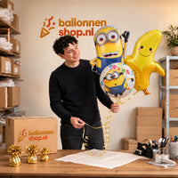 Jesse houdt Minion Trosje XL Met Banaan vast in de warme werkplaats van Ballonnenshop.nl.
