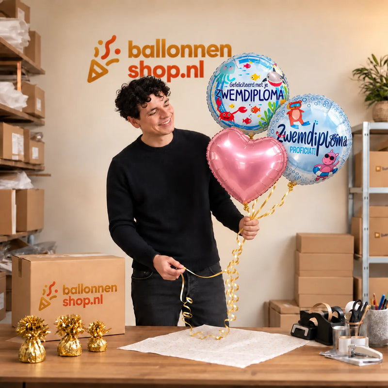 Jesse houdt Zwemdiploma Trosje Ballonnen Roze vast in de warme werkplaats van Ballonnenshop.nl.