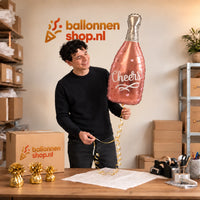 Jesse houdt de Wijnfles Cheers Helium Ballon vast in de warme inpakruimte van Ballonnenshop.nl.