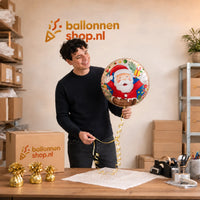 Jesse houdt de Kerstman Uit Schoorsteen Ballon vast in de warme werkplaats van Ballonnenshop.nl.